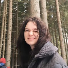 a woman standing in front of some tall trees