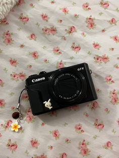 a camera sitting on top of a bed next to a flowery blanket with a keychain