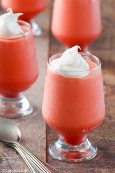 three desserts with whipped cream in small glasses on a wooden table next to spoons