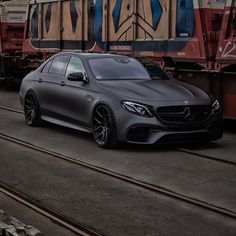 a silver car parked next to a train on the tracks in front of a train