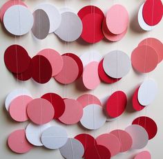 some paper circles hanging from a string on a white wall with red and pink colors