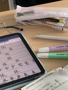 a tablet computer sitting on top of a wooden desk next to glasses and pens,