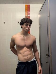 a shirtless young man standing in front of a bathroom mirror looking at the camera