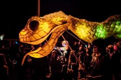 a group of people standing next to each other near a dragon shaped kite at night