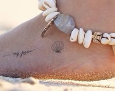 a close up of a person's foot on the beach with shells and seashells