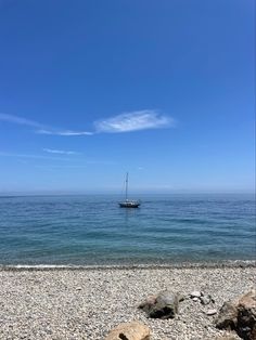 a boat is out on the water near some rocks and pebbles in the foreground