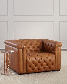 a brown leather couch sitting on top of a rug next to a glass table and white wall