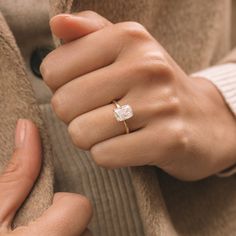 a woman's hand wearing a ring with a diamond in the middle and on her finger