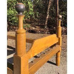 an old wooden bed frame with a ball on the headboard and foot board, in front of some trees