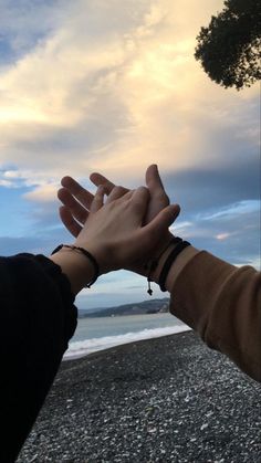 two people reaching their hands out to each other on a beach with the ocean in the background