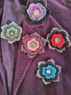 several crocheted flowers are placed on top of a purple jacket with buttons in the center