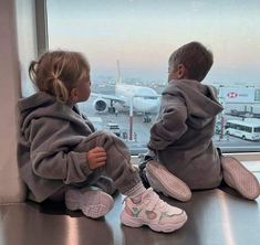 two children sitting on the window sill looking out at an airport