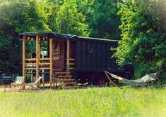 an old train caboose sits in the middle of a grassy field with hammocks hanging from it's sides