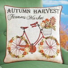 an embroidered pillow with a bicycle and flowers on it, sitting on a green chair