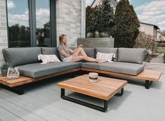 a woman sitting on top of a gray couch next to a wooden table and coffee table