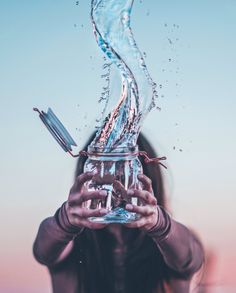 a woman is holding up a glass with water pouring out of it to her face