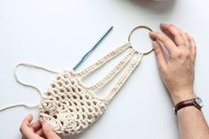 two hands are holding crocheted purses on a table with yarn and scissors