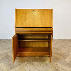 a small wooden cabinet sitting on top of a hard wood floor next to a white brick wall