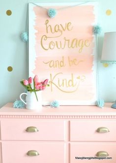 a pink dresser topped with a white vase filled with flowers next to a sign that says have courage and be kind