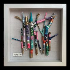 a shadow box frame with several different types of beads and pens in it that are hanging on the wall