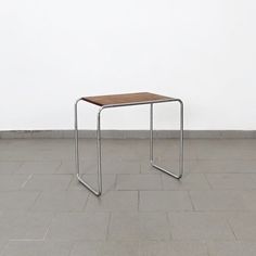 a wooden table sitting on top of a tile floor next to a white wall in an empty room