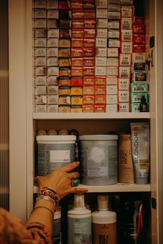 a person is reaching for some medicine in a cabinet with many bottles and containers on the shelves