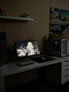 a desk with a computer monitor, keyboard and mouse on it in front of a painting