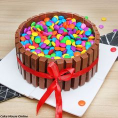 a chocolate cake with colorful candy toppings on top and a red ribbon around the edge