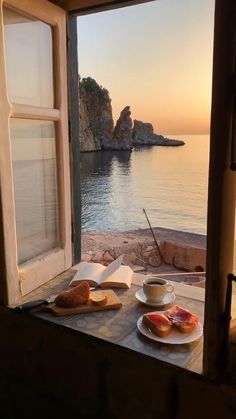 an open window overlooking the ocean with bread and coffee