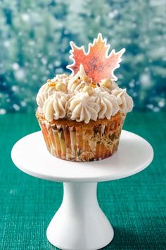 a cupcake with frosting and an autumn leaf on top sits on a cake stand