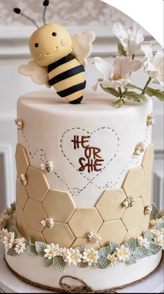 a white cake with a bee on top and flowers around the edges that say he or she