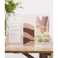 two cards with hands holding each other on a table next to a vase filled with flowers