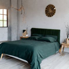 a bed with green sheets and pillows in a room next to a clock on the wall