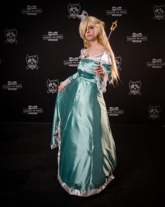 a woman in a green dress holding a wand and posing for a photo on a black background