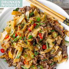 a white plate topped with noodles and meat next to chopsticks on a wooden table