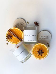 an orange and cinnamon candle next to some spices on a white surface with two round containers