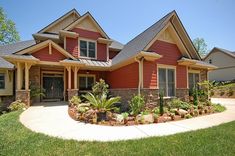 a large red house with lots of windows and plants in the front yard, on a sunny day