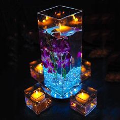 an illuminated vase with candles and flowers in it