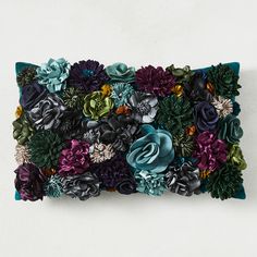 a decorative pillow made out of flowers on a white wall with green and purple accents