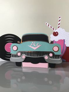 an old fashioned car with a cupcake and candy on the hood is sitting in front of a record player