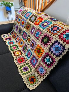 a crocheted granny granny blanket sitting on top of a couch next to a stair case