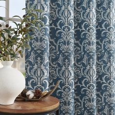 a white vase sitting on top of a wooden table next to a blue and white curtain