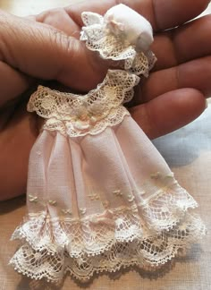 a hand holding a small doll with white lace on it's dress and headband