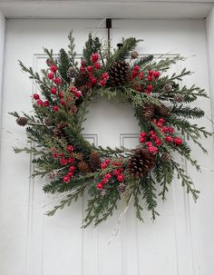 a wreath with pine cones and berries hanging on a door