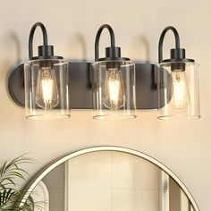 three light bathroom fixture with clear glass shades and black metal frame, on a white wall