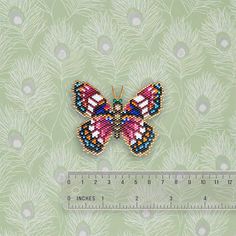 a beaded butterfly sitting on top of a green wall next to a measuring ruler