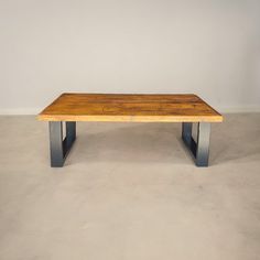 a wooden table sitting on top of a cement floor next to a white wall in an empty room