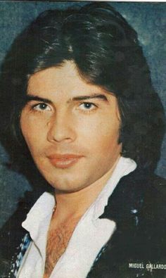 an old photo of a young man with long hair and black blazer, looking at the camera