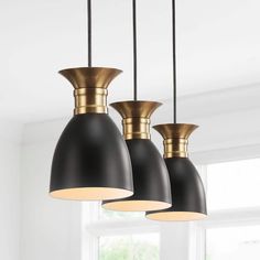 three black and gold pendant lights hanging from the ceiling in a white room with windows