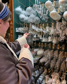 a woman is looking at glass ornaments on display in a store window, with other items hanging from the wall behind her